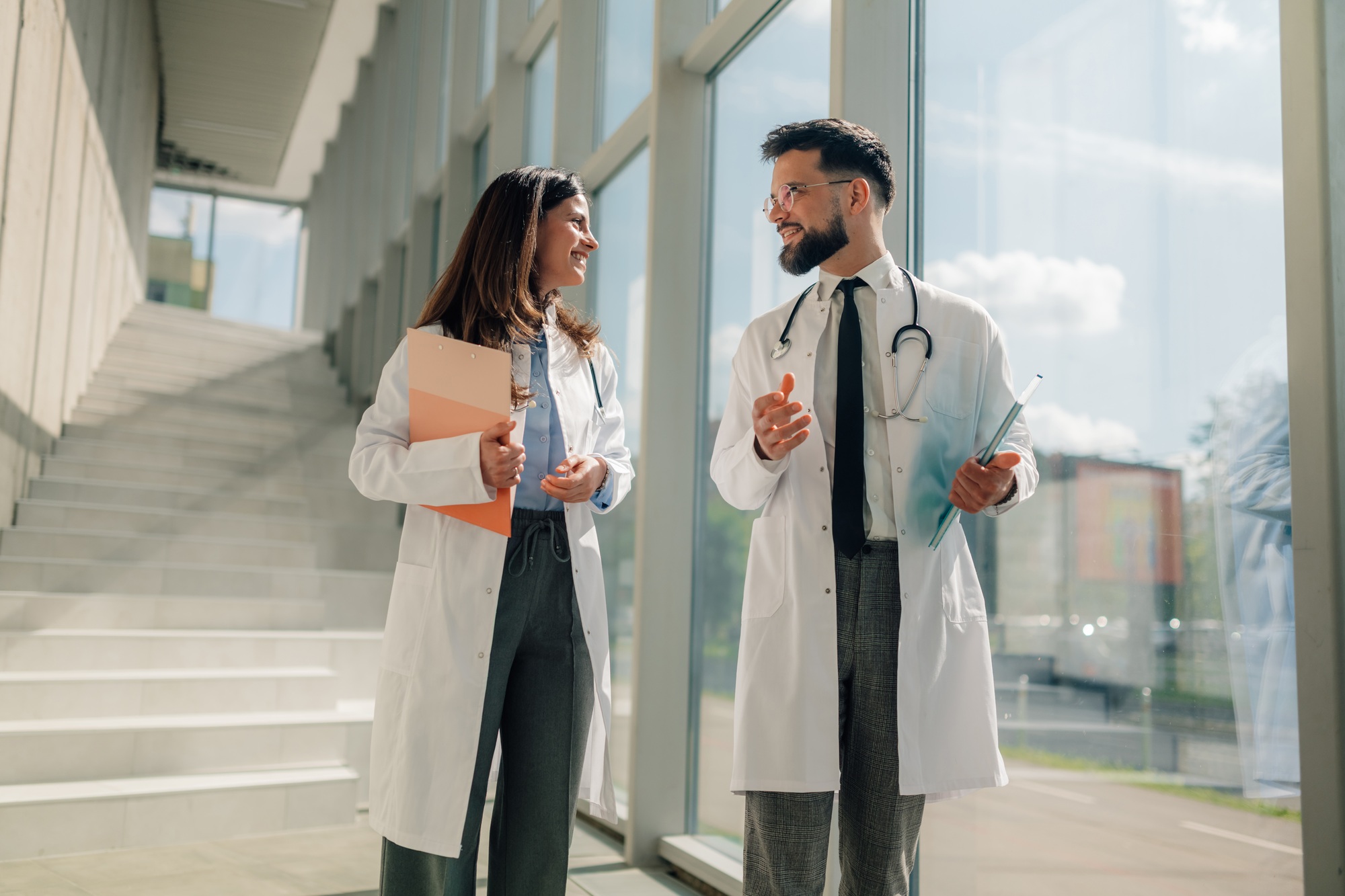 Two healthcare professionals in white coats conversing in a sunlit hallway at Multicare Wellness, reflecting a collaborative and modern medical environment – About Multicare Wellness